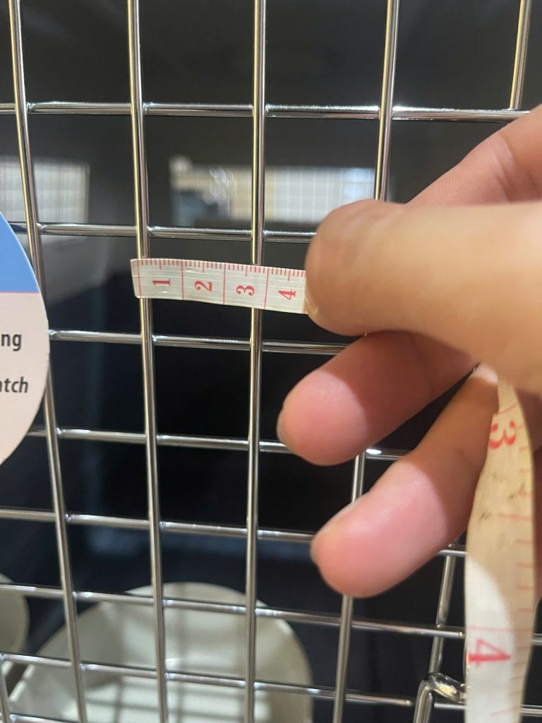 Tape measure held across the metal window of a pet crate, showing an opening of about 2.5 cm